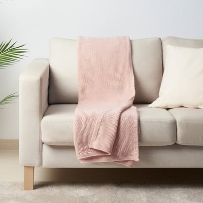 Hellrosa HUMLEMOTT Decke auf neutraler Couch, weich, gestrickt, gemütlich, mittelgroß.