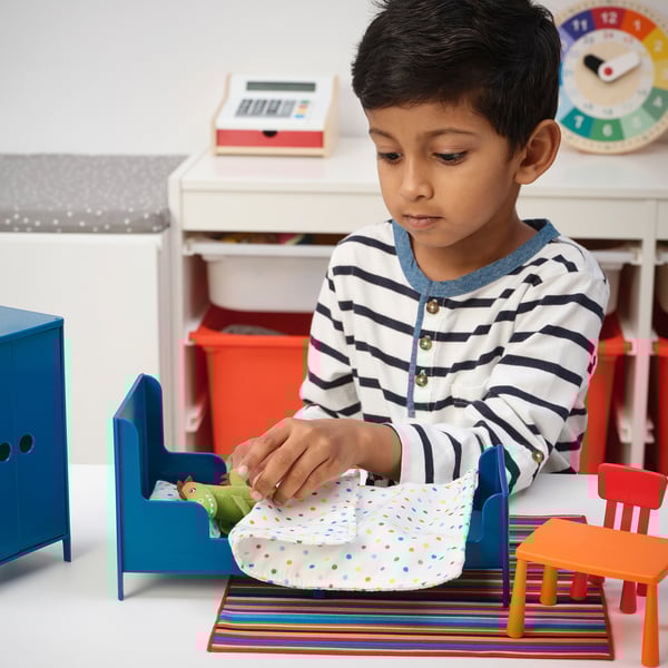 Ein Junge, der mit einem Miniaturmöbelset spielt, stellt eine Spielzeugfigur in ein Bett.