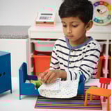 Ein Junge, der mit einem Miniaturmöbelset spielt, stellt eine Spielzeugfigur in ein Bett.