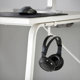 Ein weißer Gaming-Schreibtisch mit einem Mauspad und einer Maus darauf. Darunter hält ein Haken einen schwarzen Kopfhörer.