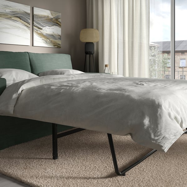 Modernes graues Schlafsofa in der Nähe eines großen Fensters mit Vorhängen, mit klaren Linien und einem bequemen, wendbaren Kissen.