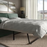 Modernes graues Schlafsofa in der Nähe eines großen Fensters mit Vorhängen, mit klaren Linien und einem bequemen, wendbaren Kissen.