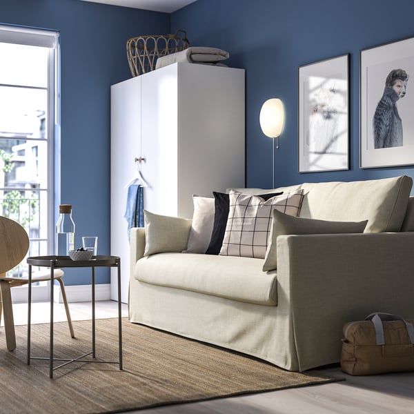 Modernes Wohnzimmer mit HYLTARP-Schlafsofa, blauen Wänden, eleganten Möbeln, Hundebildern und Tageslicht.