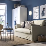 Modernes Wohnzimmer mit HYLTARP-Schlafsofa, blauen Wänden, eleganten Möbeln, Hundebildern und Tageslicht.