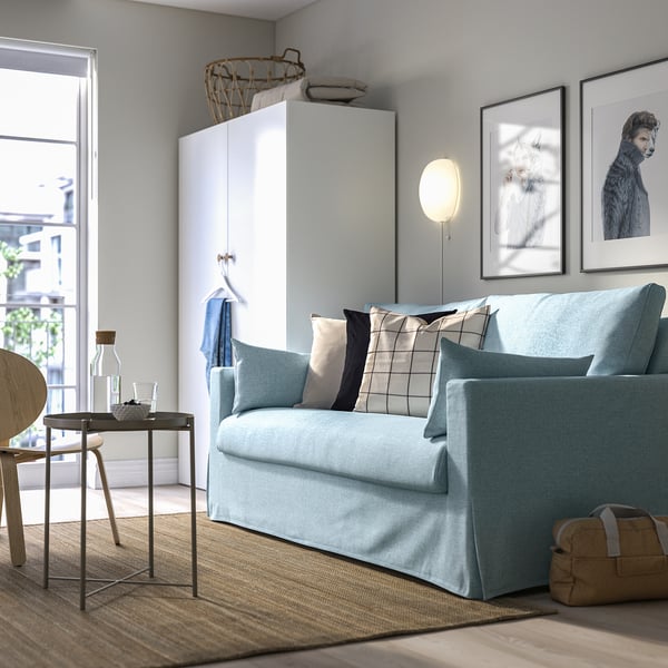 Hellblaues HYLTARP-Sofa vor großem weißem Schrank, gerahmte Kunstwerke in der Nähe.