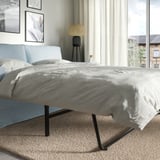 Bett in modernem Zimmer, ausziehbares Sofa mit Kissen, Stoffbezug, Metallbeine, in der Nähe des Fensters.