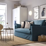 Modernes blaues Sofa mit bunten Kissen im hellen Wohnzimmer. Groß, gemütlich, mit Fenster und Kunstwerken dahinter.