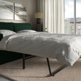 Modernes Schlafzimmer mit grauer Bettwäsche, grünem Kopfteil und Stehlampe. Fenster mit Blick auf die Stadt.