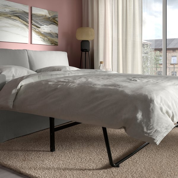 Modernes Schlafzimmer mit rosa Wänden, grauem Schlafsofa, schwarzen Beinen, Lichtvorhang, Nachttisch, Lampe und abstrakter Kunst. Perfekt zum Entspannen oder Schlafen.