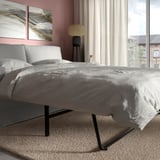 Modernes Schlafzimmer mit rosa Wänden, grauem Schlafsofa, schwarzen Beinen, Lichtvorhang, Nachttisch, Lampe und abstrakter Kunst. Perfekt zum Entspannen oder Schlafen.
