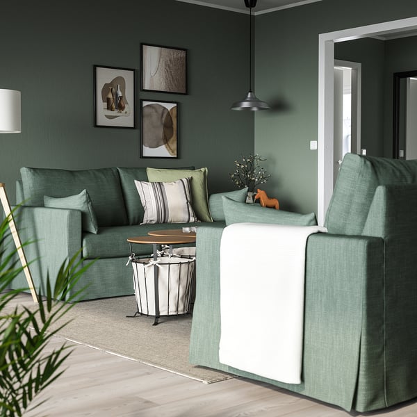 Modernes Wohnzimmer mit grünem HYLTARP-Sofa, weißer Ottomane, schwarzer Pendelleuchte, Kunstwerk und einem Beistelltisch.