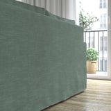 Ein gemütliches grünes Sofa mit wendbaren Kissen steht in der Nähe eines Balkonfensters und zeigt sein komfortables Design und seinen leicht zu reinigenden Bezug.