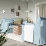 Modernes Wohnzimmer mit hellblauem, l-förmigem HYLTARP-Sofa, Couchtisch aus hellem Holz und Wandkunst. Das Sofa ist groß, die Ecke passt gut.