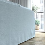 Ein hellblaues Sofa in einem hellen Raum in der Nähe eines Fensters, das seine klaren Linien, weichen Kissen und einladenden Komfort zur Geltung bringt.