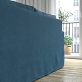 Blaues Sofa mit hochelastischem Schaumstoff und Taschenfedern für Komfort, wendbaren Kissen und maschinenwaschbarem Bezug. In der Nähe eines Fensters mit Pflanzen.
