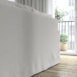 Ein hellgraues Sofa in der Nähe eines Fensters mit Pflanzen und einem Balkon, das sein klares Design und seine bequemen Kissen zur Geltung bringt.