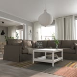 Modernes Wohnzimmer mit großem braunem L-Sofa, weißem Couchtisch, buntem Teppich, grauen Vorhängen und einer großen Hängelampe.