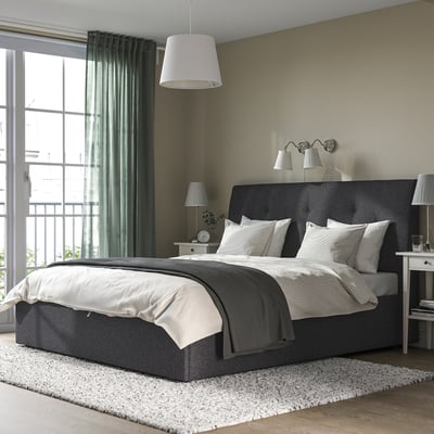 Modernes Schlafzimmer mit IDANÄS-Bett, Stauraum unter dem Bett und großem Fenster, das von weißen Vorhängen eingerahmt ist.