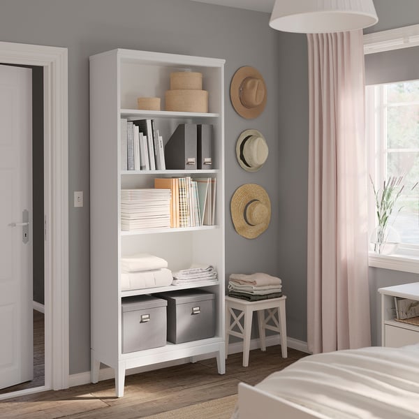 Modernes Schlafzimmer mit weißem IDANÄS-Bücherregal, Hüten und gefalteter Kleidung.