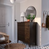 Eingangsbereich mit IDANÄS Kommode aus dunklem Holz, rundem Spiegel, Lampe, Pflanze, Kleiderhaken.