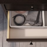 Offene Holzschublade mit Metallgriff, in der sich ein gerollter schwarzer Gürtel und graue Kleidung befinden.