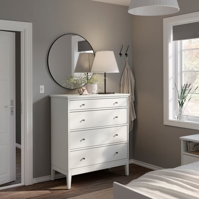 Modernes Schlafzimmer mit weißer IDANÄS-Kommode, rundem Spiegel, Lampe und Kleiderhaken. Klares, minimalistisches Design.