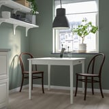 Modernes, kompaktes Home Office mit weißem Klapptisch und braunen Stühlen, grünen Wänden und großem Fenster.