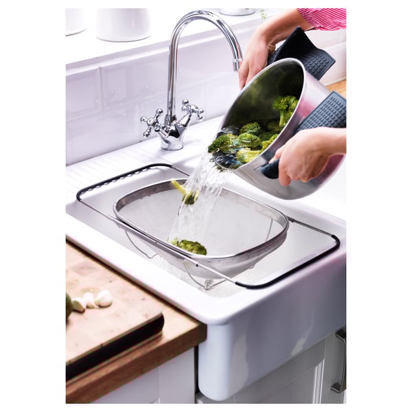 Die Person gießt Wasser in das Sieb für Brokkoli.