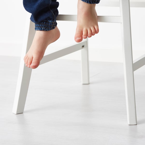 Die nackten Füße des Kindes hängen an einem weißen Juniorstuhl und zeigen seine Fußstütze.