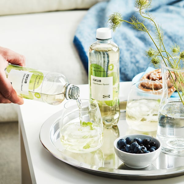Gießen Sie das Getränk mit ISKUB-Holunderblütengeschmack von Hand in ein Glas mit Eis, das Tablett enthält auch ein weiteres Glas mit Blaubeeren und Beeren, die Flasche steht in der Nähe.