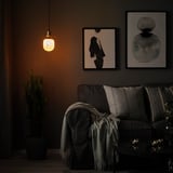 Gemütliches Wohnzimmer mit dunklen Möbeln, warmer Lampe, grauer Couch, Wandkunst, Pflanze und Kerzen.