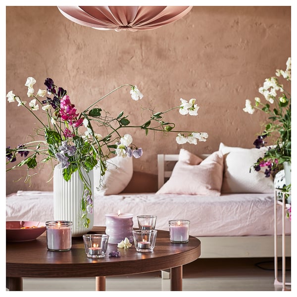 Gemütliches Wohnzimmer mit rosa Kissen, Blumen und brennenden Kerzen.