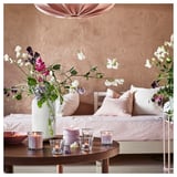 Gemütliches Wohnzimmer mit rosa Kissen, Blumen und brennenden Kerzen.