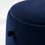 Ein dunkelblauer gepolsterter Hocker mit einem schlanken, geschwungenen Design und sichtbaren Nahtdetails, der gut verarbeitet und stilvoll wirkt.