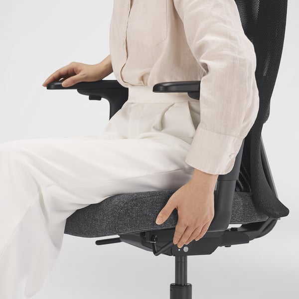 Person, die ergonomischen Bürostuhl einstellt, mit gezielter Lendenwirbelstütze. Der Stuhl hat eine Netzrückenlehne, einen höhenverstellbaren Sitz und eine Neigungssperre.