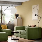 Modernes Wohnzimmer mit grüner JÄTTEBO-Sofagarnitur, gelben Kissen, schwarzer Stehleuchte und beiger Wandkunst.