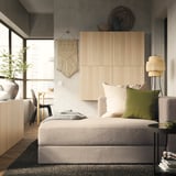 Modernes Schlafzimmer mit JÄTTEBO-Sofa in neutralen Tönen, Holzpaneelen und Makramee-Wandbehang, das eine gemütliche und minimalistische Ästhetik bietet.