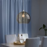 Moderne Esseinrichtung mit Rauchglaslicht, weißen Stühlen, klaren Gläsern, Holztablett und Vase. Vorhänge zugezogen.