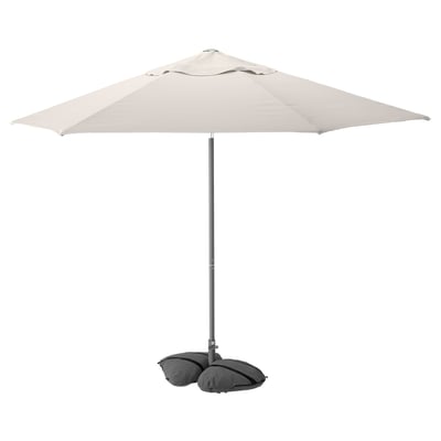JOGGESÖ cremefarbener Outdoor-Regenschirm mit Kippe, Aluminiumstange, graue Sandsäcke.