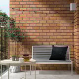 Moderne Balkoneinrichtung mit grauem JOLPEN-Outdoor-Sofa vor Backsteinwand, kleinem runden Beistelltisch mit Teeservice, schwarzem Kissen und Topfpflanze.