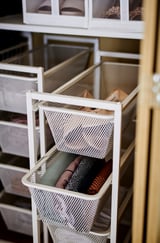 Organisierte Regale mit JONAXEL-Behältern aus weißem Netz, in denen ordentlich gefaltete Kleidung und Accessoires Platz finden. Die Behälter gleiten leichtgängig und lassen die Luft zirkulieren.