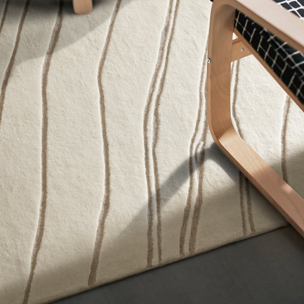Ein weicher, beigefarbener und brauner Teppich mit Wellenmuster und Holzstuhl, der an die Ruhe des Strandes erinnert, mit einer weichen, sinkenden Textur.