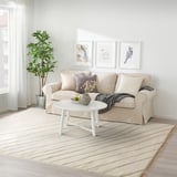 Ein Wohnzimmer mit einem beigen Teppich von JULGRANSGRÄS, einem beigen Sofa und Wandkunst zum Thema Natur.