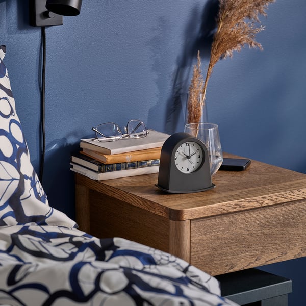 Nachttisch mit Uhr, Gläsern, Büchern, Telefon und Vase. Die Uhr zeigt die Zeit mit leuchtenden Spitzen an, Steine zum Aufwachen.