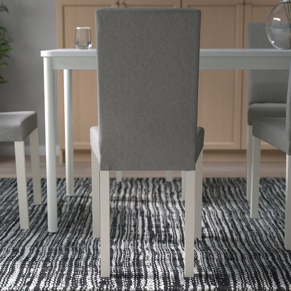 Moderner Esszimmerstuhl mit grau gepolsterter Rückenlehne und Sitzfläche, hoher Rückenlehne für Komfort, um einen Tisch mit gestreiftem Teppich angeordnet.
