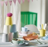 Buntes Geschirrset aus Kunststoff, bestehend aus gestapelten Tassen, Schüsseln mit Lebensmitteln und Utensilien, für Kinder, die lernen, selbstständig zu essen.