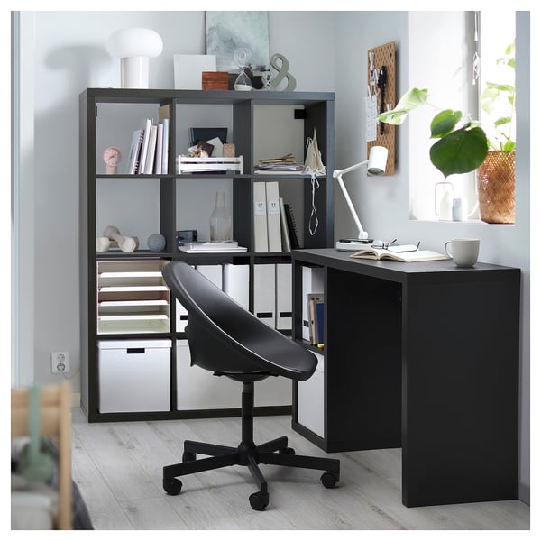 Schwarzer Schreibtisch mit KALLAX Regal, Pflanzen, Büchern und Lampe.