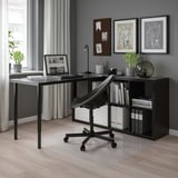 Moderne Home-Office-Einrichtung mit schwarzen KALLAX Regalen, Schreibtisch, Stuhl, Laptop und Dekor. Graue Wände, großes Fenster.