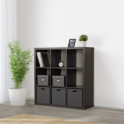 Schwarzes KALLAX-Regal mit grauen Behältern und weißer Uhr, Pflanze und Büchern.