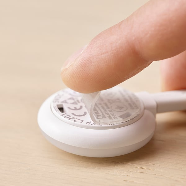 Eine Hand drückt auf einen runden weißen Kaplake-Strahler mit einem klebrigen Gel-Pad, was seine einfache Installation und Steuerung unterstreicht.